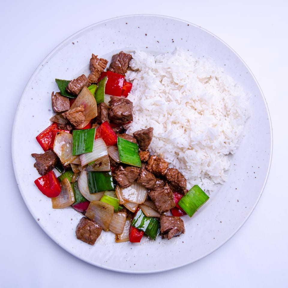 Everything Noodles' beef stir-fry with red peppers, onions, and green onions, served with white rice.