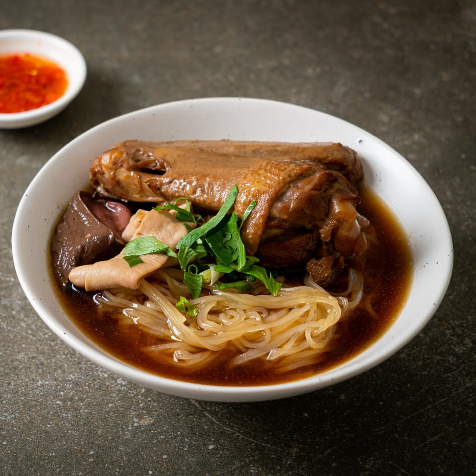 A bowl of Everything Noodles' braised chicken with glass noodles, blood curd, and herbs.