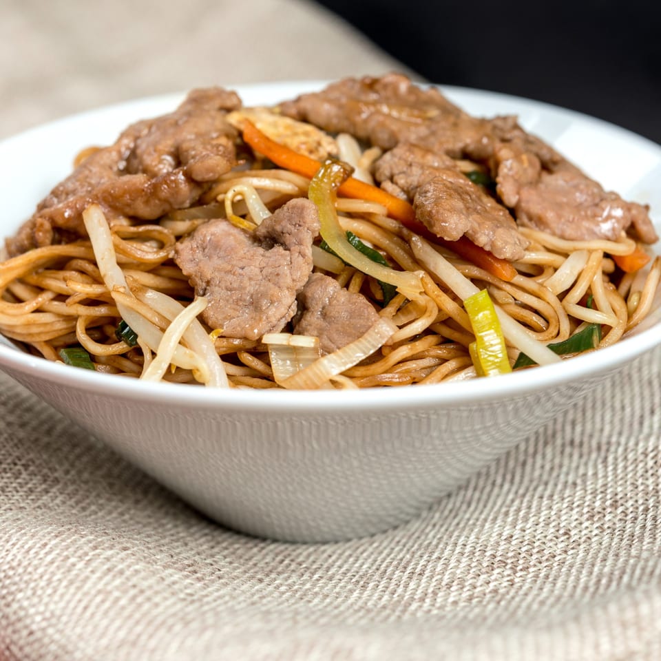 Everything Noodles' beef chow mein with noodles, beef, bean sprouts, carrots, and onions in a white bowl.